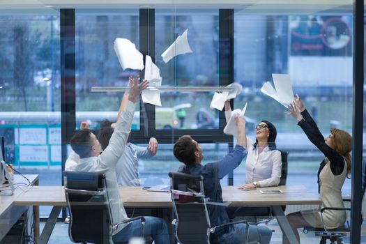 Group of young business people throwing documents and looking happy while celebrating success at their working places in startup office