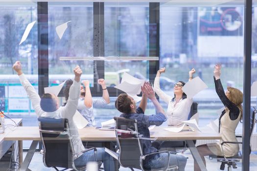 Group of young business people throwing documents and looking happy while celebrating success at their working places in startup office