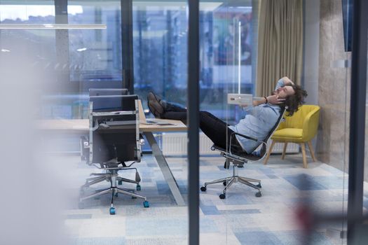 A time for relax. Young tired casual businessman relaxing at the desk in his office