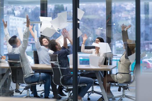 Group of young business people throwing documents and looking happy while celebrating success at their working places in startup office