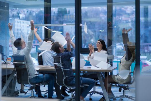 Group of young business people throwing documents and looking happy while celebrating success at their working places in startup office