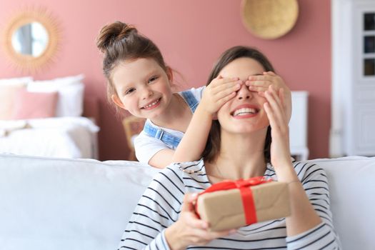 Little girl make birthday present to excited parent , smiling little child congratulate give gift box to happy mother and closed mother's eyes