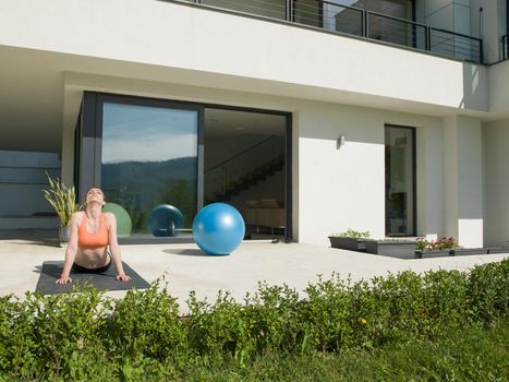 young handsome woman doing morning yoga exercises in front of her luxury home villa