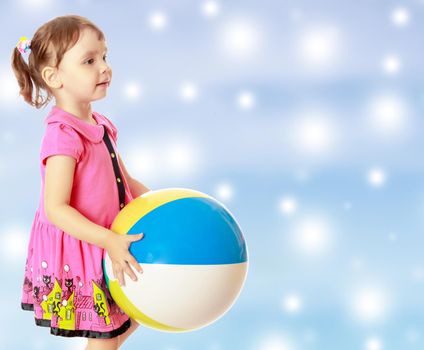 Beautiful little girl in a pink dress throwing a big striped ball. Turned sideways. Close-up.On new year or Christmas blue background with white big stars.