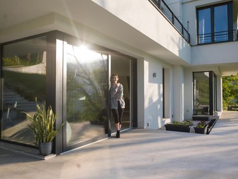 portrait of a young beautiful successful woman drinking coffee in the doorway of her luxury home villa