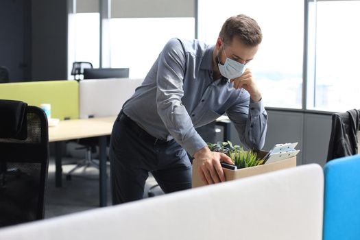 Dismissal employee in an epidemic coronavirus covid-19. Sad dismissed worker are taking his office supplies with him from office