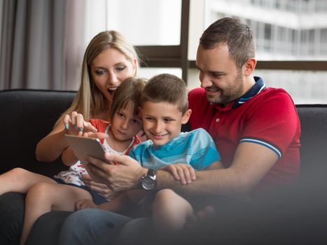 Happy Young Family Playing Together with tablet at home sitting on the sofa