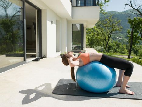 young beautiful woman doing exercise with pilates ball in front of her luxury home villa