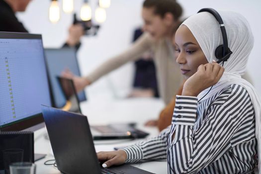 beautiful modern african Muslim businesswoman in office, wearing hijab speaking on headset at modern startup coworking space