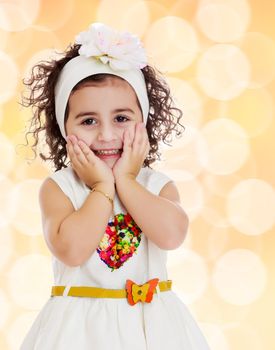 Beautiful little curly girl in a white dress happily surprised. Girl holding hands near the face. Close-up.Winter brown abstract background with white snowflakes.