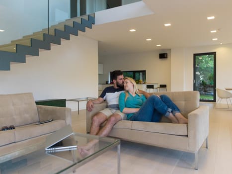 Young couple relaxes on the sofa in the luxury living room, using a laptop and remote control