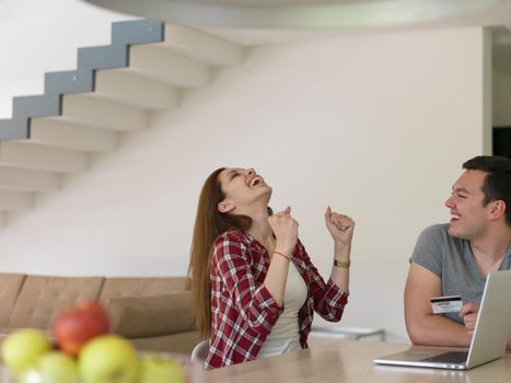 happy young couple buying online using laptop a computer and a credit card in their luxury home villa