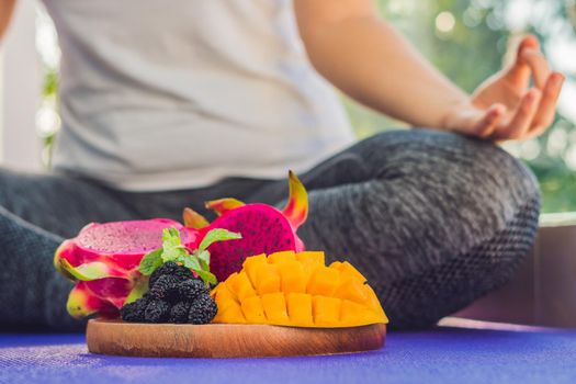 hand of a woman meditating in a yoga pose, sitting in lotus with fruits in front of her dragon fruit, mango and mulberry.
