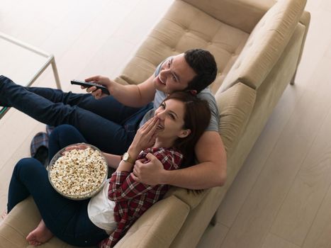 young handsome couple enjoying free time watching television with popcorn in their luxury home villa