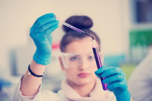 young female student with protective glasses making chemistry experiment in bright laboratory,education and medicine concept