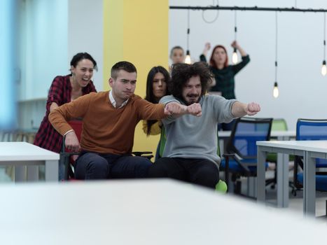 business people having fun while racing on office chairs in modern coworking open space office