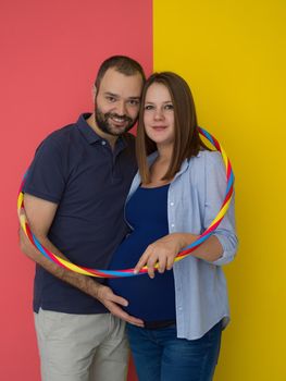 Portrait of a happy young couple,man holding his pregnant wife belly isolated over colorful background
