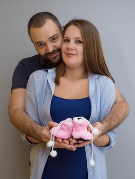 young  pregnant couple holding newborn baby shoes isolated on white background in family and parenthood concept