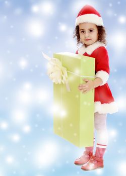 Adorable little curly-haired girl in a coat and hat of Santa Claus,holding a big green box with a gift.Blue winter background with white snowflakes.