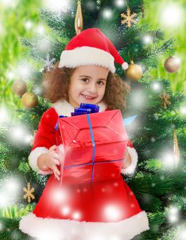 The delicate, curly little girl in a suit and hat of Santa Claus standing near Christmas tree with gift in hand.On a green background with white snowflakes.