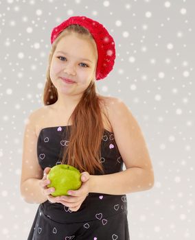 Cute little girl in fancy dress, holding a green Apple. Close-up.On the Christmas background with white snowflakes.