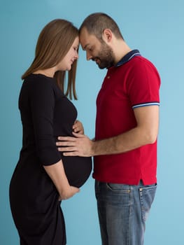 Portrait of a happy young couple,man holding his pregnant wife belly isolated over blue background