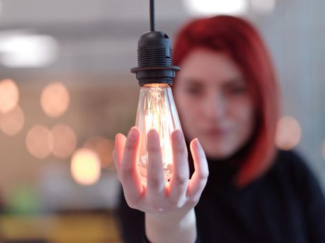 redhead businesswoman at office holding a hand around light bulb representing concept of business solutions idea and green energy