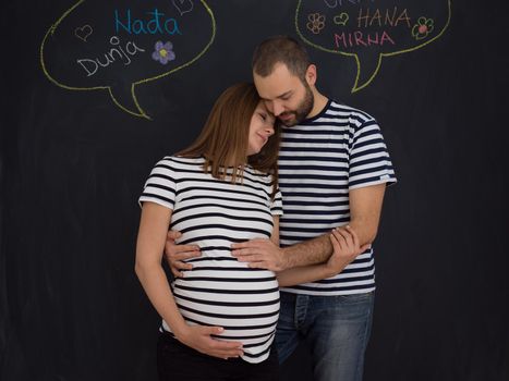 portrait of husband and pregnant wife posing against black chalk drawing board