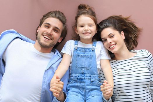 Top view portrait of smiling young parents with little preschooler daughter lying relaxing on warm floor at home, happy family with small child rest have fun at home