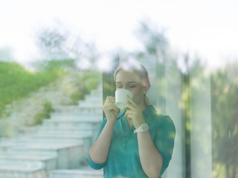 beautiful young woman drinking morning coffee by the window in her home