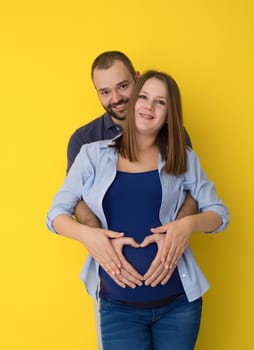 Portrait of a happy young couple,man holding his pregnant wife belly isolated over yellow background