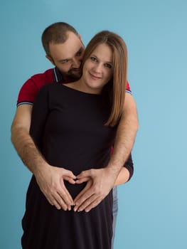 Portrait of a happy young couple,man holding his pregnant wife belly isolated over blue background