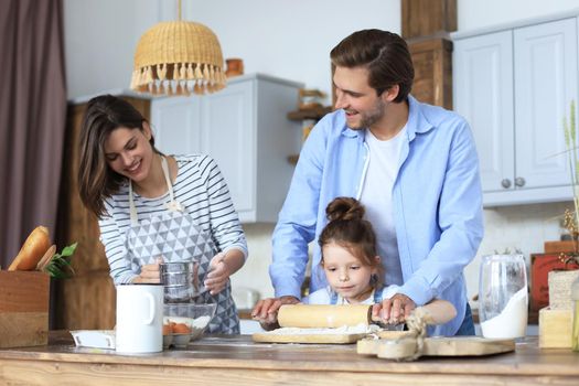 Cute little girl and her parents are having fun while cooking in kitchen at home together