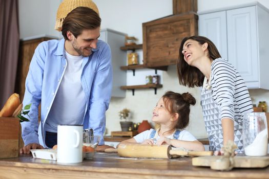 Cute little girl and her parents are having fun while cooking in kitchen at home together