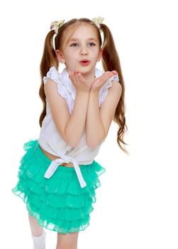 Cheerful little girl in a short green skirt and white shirt without any inscriptions . Long tails on the head in which braided white ribbons. Girl sends everyone a kiss. Close-up