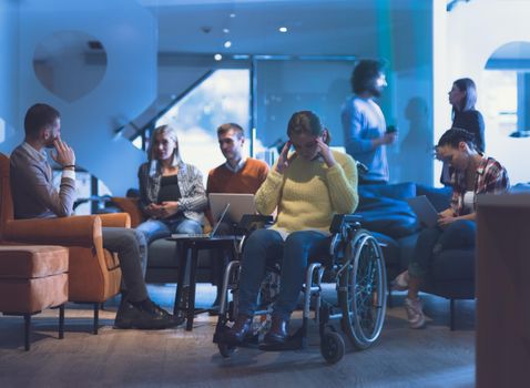 Portrait of disabled businesswoman in a wheelchair in front of her diverse business team in a modern open space coworking office space. High quality photo