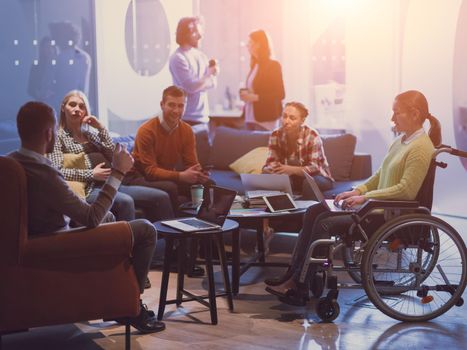 Handicapped businesswoman in a wheelchair on meeting with her diverse business team brainstorming about ideas and plans in a modern open space coworking office space. High quality photo