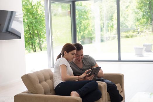 Young couple relaxing at luxurious home with tablet computers reading in the living room on the sofa couch.