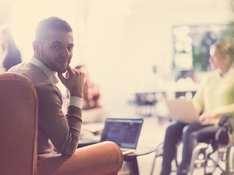 businessman using laptop at the office for remote distance meeting diverse business team in the background disabled woman in a wheelchair