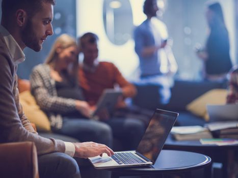 businessman using laptop at the office for remote distance meeting or watching webinar concentrated employee, analyzing project results in the distance, diverse business team in the background