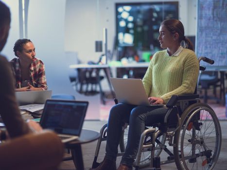 Handicapped businesswoman in a wheelchair on meeting with her diverse business team brainstorming about ideas and plans in a modern open space coworking office space. High quality photo