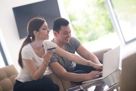 happy young couple buying online using laptop a computer and a credit card in their luxury home villa