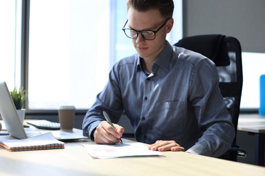 Portrait of handsome smiling man in casual shirt taking notes at workplace