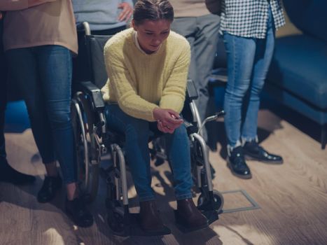 Sad and depressed disabled businesswoman in a wheelchair at the office with coworkers. Diverse business team in a modern open space coworking office space. High quality photo