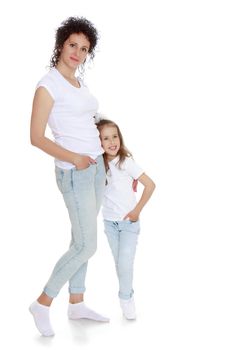 Happy, charming young mother with adorable little daughter. In the same jeans and white t-shirts without a pattern. Mother hugs daughter's waist - Isolated on white background