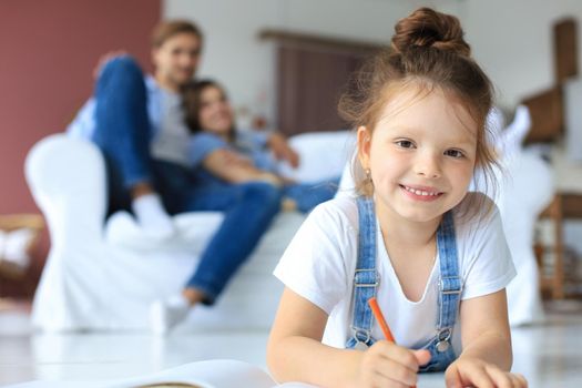 Smiling happy family sit relax on couch in living room watch little daughter drawing in album with colorful pencils. Happy weekends at home