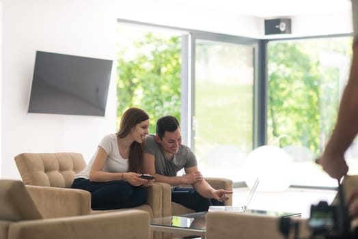 Young couple relaxing at luxurious home with tablet and laptop computers reading in the living room on the sofa couch.