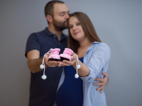 young  pregnant couple holding newborn baby shoes isolated on white background in family and parenthood concept