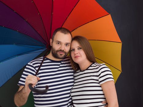 portrait of husband and pregnant wife posing with colorful umbrella in front of black chalk drawing board