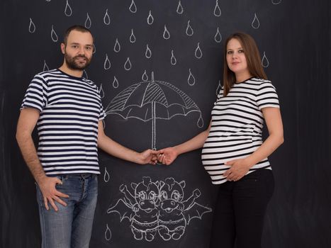 Conceptual photo of pregnant couple drawing their imaginations about the future life with children on chalk board